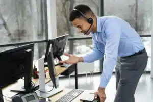 Homem de negócios usando headset e realizando suporte técnico em videochamada, no escritório moderno