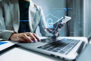 Executivo mexendo no celular com o notebook aberto, representando a segurança digital.